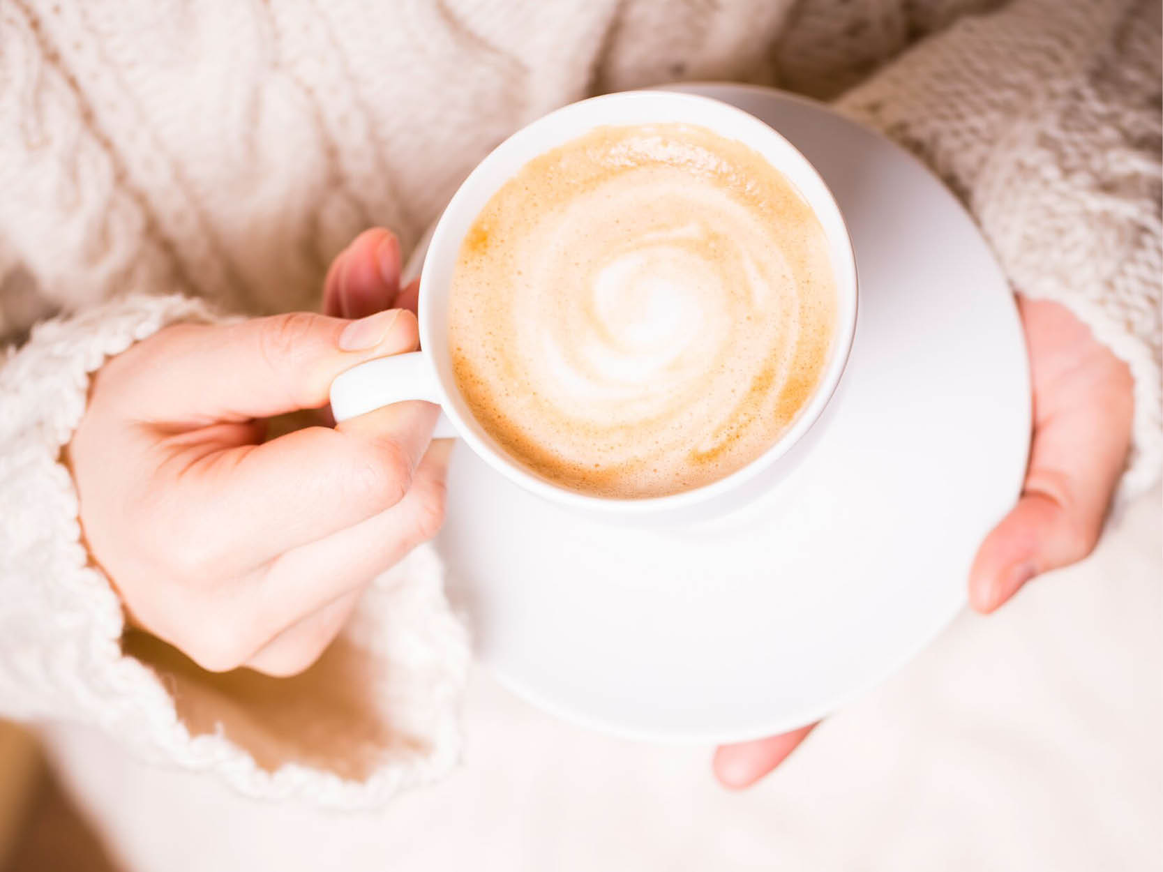 Two hands of holding a cup of coffee with milk foam on top.